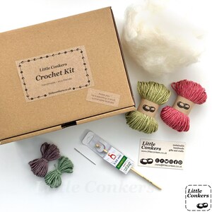 May include: A brown cardboard box labeled Little Conkers Crochet Kit, containing white stuffing, two skeins of green and pink yarn, two smaller purple and green yarn bundles, a 3.50 mm bamboo crochet hook, a metal needle, and a business card.
