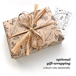May include: A rectangular gift box wrapped in tan paper featuring a black line-art pattern of leaves, acorns, and berries. The package is tied with a tan raffia ribbon and includes a small white card printed with the text a gift for you.