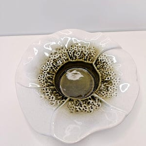 May include: A ceramic bowl shaped like a flower with white, smooth petals and a textured, dark olive green center. The glaze in the middle features a bubbly, cratered appearance that transitions into the glossy white finish of the outer rim.
