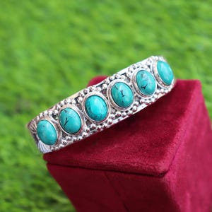 May include: A silver cuff bracelet featuring five oval-shaped turquoise stones with dark veining. The metal band is decorated with a beaded texture along the edges and engraved patterns on the sides, showcasing a polished metallic finish throughout.