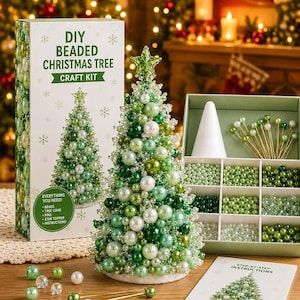 Op de afbeelding: Een DIY-knutselpakket voor een kerstboom van kralen met een witte doos met groene tekst, een volledig gemonteerde groen-witte kralenboom met een ster als piek, een verdeelbak met kralen, gouden spelden en een stapsgewijze instructiekaart.