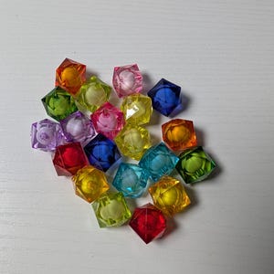 May include: A collection of small, multi-colored translucent beads with a faceted, geometric cube shape. The beads appear in various vibrant hues including red, blue, green, yellow, orange, pink, and purple, each featuring a central circular hole.