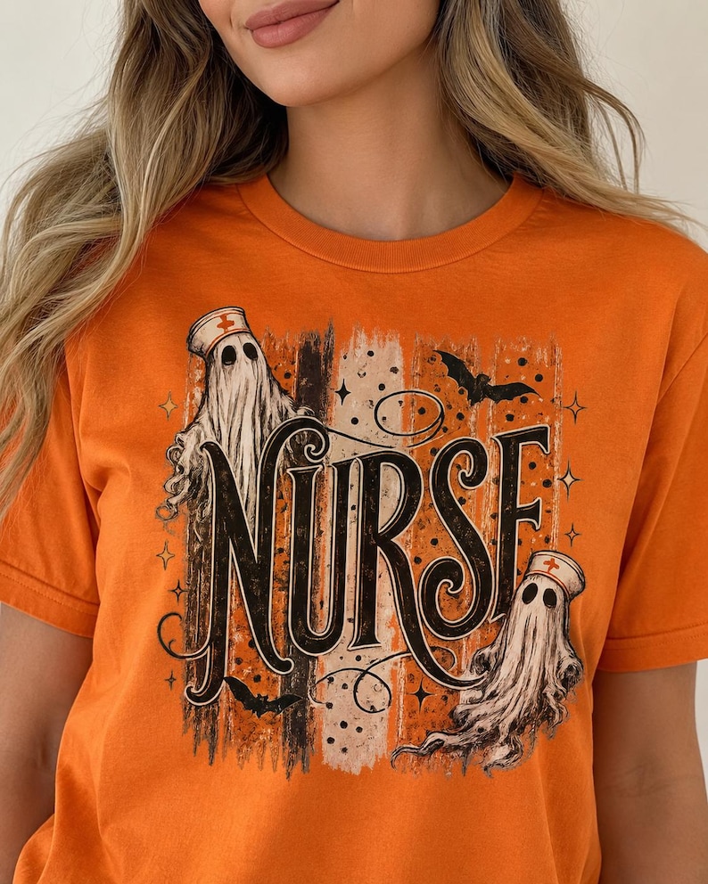 May include: An orange short-sleeved t-shirt featuring a graphic print with the word NURSE in large black letters. The design includes two white ghosts wearing nurse caps, small black bats, and vertical distressed stripes in black and tan.
