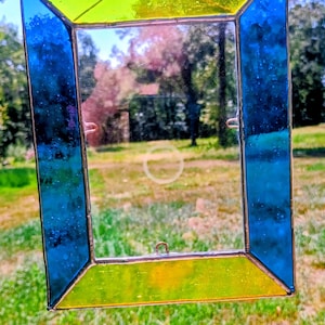 May include: A rectangular stained glass frame featuring vibrant lime green glass panels on the top and bottom, complemented by deep blue glass panels on the left and right sides. The frame is held together by thin metal solder lines and includes small metal loops.