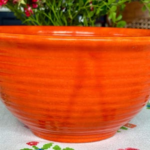 May include: A vibrant orange ceramic mixing bowl featuring a glossy finish and horizontal ribbed texture along the exterior walls. The bowl has a wide, open circular rim and a deep, rounded basin, showcasing a consistent, bright solid color throughout.
