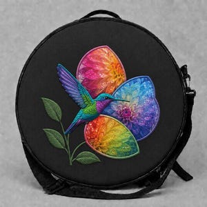 May include: A round black bag featuring an embroidered design of a vibrant hummingbird in shades of blue, green, and purple, perched on a green stem with leaves, surrounded by three colorful, textured floral shapes in rainbow gradients.