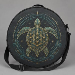 May include: A round black shoulder bag featuring a central graphic of a sea turtle with a golden flower of life pattern on its shell. The turtle is surrounded by teal swirling water motifs, golden stars, and thin lines on a dark background.