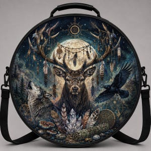 May include: A round black crossbody bag featuring a detailed graphic print of a deer with large antlers, a howling wolf, and a flying raven. The design includes a full moon, hanging feathers, crystals, and geometric symbols on a dark forest background.