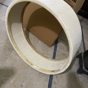 Op de afbeelding: Een groot, cirkelvormig oefenwiel gemaakt van lichtgekleurd multiplex met een glad, gebogen oppervlak. De structuur heeft een brede, holle binnenkant met zichtbare houtnerfpatronen en verstevigde randen langs de binnenste ring.