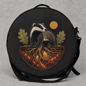 May include: A round black bag featuring an embroidered design of a badger standing above exposed tree roots. The roots contain glowing orange lava and yellow crystals. Two green oak leaves flank the badger, and a small yellow circle sits above.