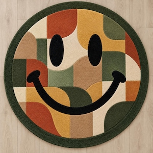 May include: A circular area rug featuring a large smiley face design composed of a geometric patchwork pattern. The rug displays a color palette of dark green, mustard yellow, burnt orange, beige, and tan, with black eyes and a curved mouth.