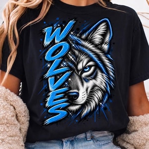 May include: A black t-shirt featuring a graphic print of a wolf's face on the right side and the word WOLVES written in large, stylized, bright blue letters on the left side. The wolf has white fur, a black nose, and a piercing blue eye.