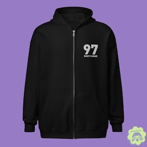 May include: A black zip-up hoodie featuring a hood, long sleeves, and a front zipper closure. The upper left chest displays the white text 97 followed by the words BAIS'S NAME printed in a clean, sans-serif font on the solid black fabric.