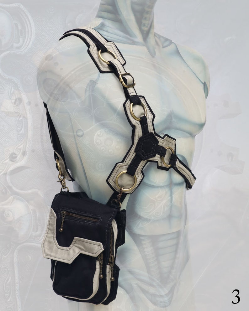 Pode incluir: Uma bolsa transversal de lona preta e branca com um design geom&eacute;trico e v&aacute;rios bolsos. A bolsa &eacute; usada no ombro de um manequim com uma al&ccedil;a branca e preta.