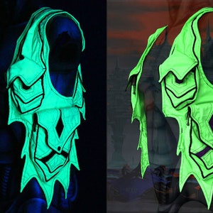 May include: A green vest with black trim and multiple pockets. The vest has a unique design with a jagged edge and a diamond-shaped pocket in the center. The vest is glowing in the dark.