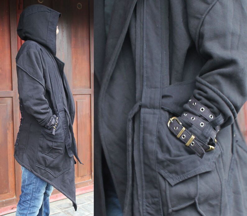 May include: A black hooded jacket with a long, asymmetrical hemline and a drawstring waist. The jacket has a zipper closure and multiple pockets. The sleeves have a unique design with multiple straps and buckles.
