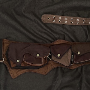 May include: A brown leather utility belt with multiple pockets and a long belt strap. The belt features a silver buckle, metal rivets, and snap closures. The pockets are various shades of brown.