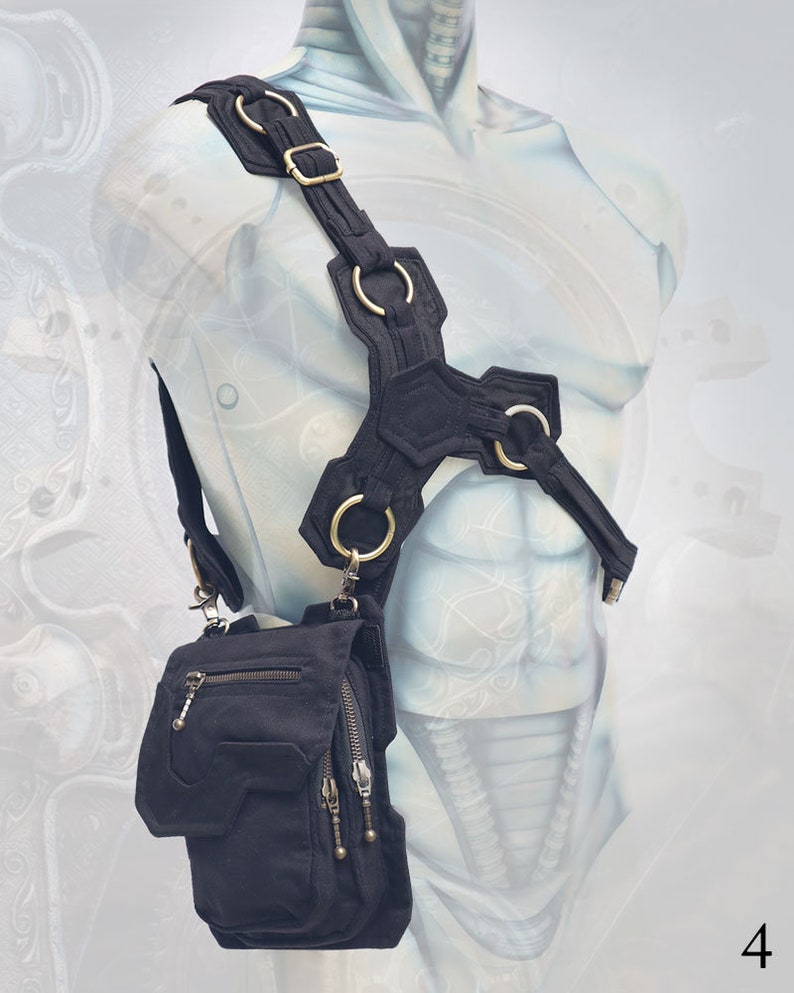 Pode incluir: Uma bolsa de ombro de lona preta com v&aacute;rios bolsos e fechos de correr. A bolsa est&aacute; presa a um arn&ecirc;s preto e prateado com v&aacute;rios an&eacute;is de metal.
