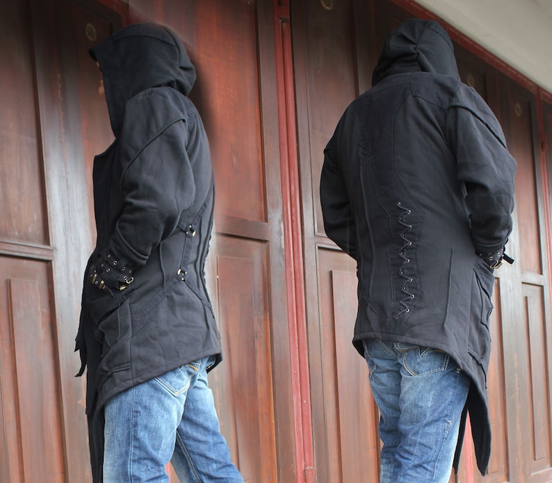 May include: A black hooded jacket with a long, asymmetrical hemline and a zipper closure. The jacket has a drawstring hood and a series of decorative laces on the back.
