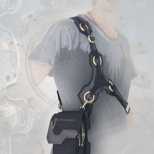 Pode incluir: Uma bolsa de ombro de couro preto com um design de al&ccedil;a exclusivo com v&aacute;rios an&eacute;is de metal. A bolsa tem um fecho de z&iacute;per e uma aba com uma fivela.