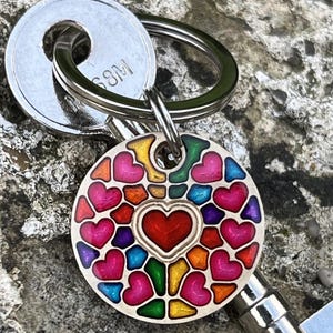 Peut inclure: Une étiquette de porte-clés ronde en métal avec un motif mosaïque coloré de cœurs dans des tons de rouge, rose, orange, jaune, vert, bleu et violet. Le centre présente un cœur rouge proéminent, attaché à un anneau fendu en argent.