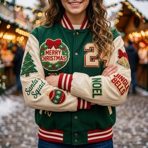 Könnte beinhalten: Eine grün-cremefarbene Collegejacke mit gestickten Weihnachtsaufnähern, darunter ein Kranz mit dem Text Merry Christmas, ein Baum, eine rote Kugel, Glocken sowie die Schriftzüge Santa's Squad, Noel und Jingle Bells und die Zahl 24.
