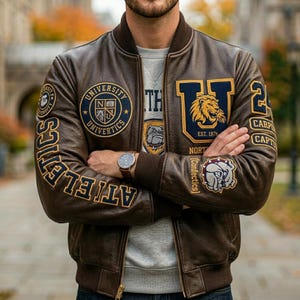 May include: A brown leather varsity jacket featuring dark blue and gold patches, including a lion emblem, a bulldog mascot, and the text University Univertics, Athletics, and Confectics. The jacket has a ribbed collar and cuffs.