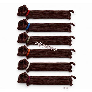 May include: Six brown crocheted dachshund bookmarks arranged vertically. Each dog has a distinctively colored collar in red, blue, green, orange, white, or purple. The text "pdf pattern" is centered, and "By Juju" is in the bottom right corner.