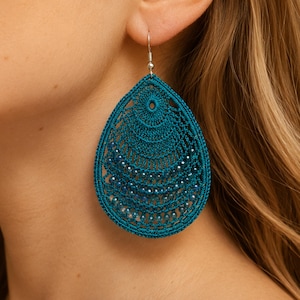 May include: A teardrop-shaped earring crafted from dark teal thread in an intricate crochet pattern. The design features concentric layers of fine stitching and small, embedded metallic beads that catch the light, suspended from a silver-toned hook.