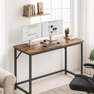 May include: A rectangular desk with a dark brown wood-grain surface and a black metal frame. The desk holds two computer monitors, a keyboard, a mouse, a small potted plant, and a pair of glasses. The frame features diagonal support braces.