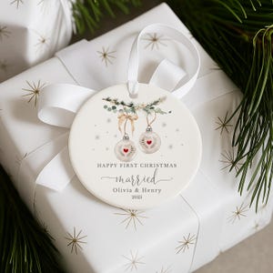 Round white ceramic ornament placed on a gift wrapped in white paper with a white satin bow and pine needles.