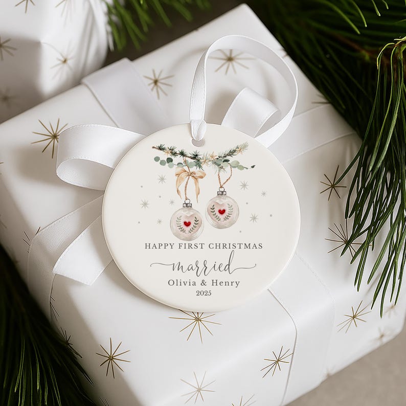 Round white ceramic ornament resting on a gift wrapped in white paper with gold star patterns and a white ribbon.
