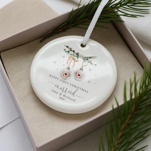Round white ceramic ornament inside a presentation box with pine needles.