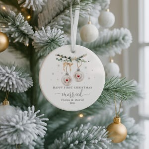 Round white ceramic ornament hanging on a snowy Christmas tree branch with gold and white baubles.
