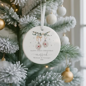 Round white ceramic ornament hanging on a frosted Christmas tree with other decorations.