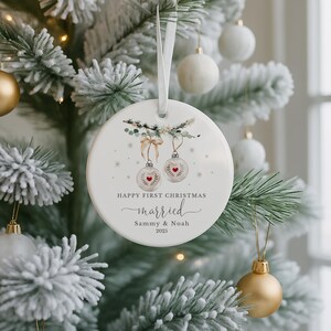 Round white ceramic ornament hanging on a snowy artificial Christmas tree.