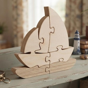 May include: A light-colored wooden sailboat puzzle composed of several interlocking pieces. The structure features a hull, a deck, and two sails, all crafted from natural plywood with visible grain patterns, standing upright as a decorative object.