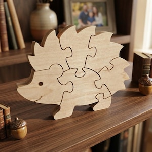 May include: A light brown wooden jigsaw puzzle shaped like a hedgehog. The puzzle is composed of several interlocking pieces that form the silhouette of the animal, featuring a smooth finish and a simple, carved eye and mouth detail on the front piece.