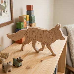 Może przedstawiać: Jasnobrązowe drewniane puzzle w kształcie lisa, składające się z kilku zazębiających się elementów. Lis jest przedstawiony w pozycji stojącej, w trakcie chodu, z długim ogonem. Słoje drewna są widoczne na powierzchni elementów, które po złożeniu tworzą kształt zwierzęcia.