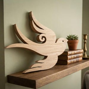 Puede incluir: Una decoración de pared de madera de color marrón claro con forma de pájaro estilizado en vuelo. El recorte presenta líneas suaves y curvas que forman las alas y la cola, con un pequeño detalle de ojo circular. Se aprecia la veta natural.