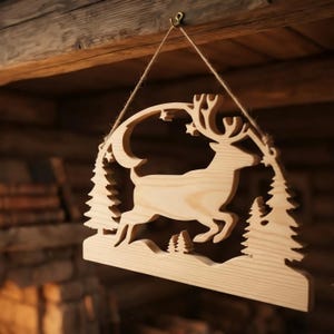 Puede incluir: Un adorno de pared de madera clara con un diseño recortado que muestra un ciervo saltando, pinos, una luna creciente y pequeñas estrellas. El adorno está suspendido por un cordel fino sujeto a un pequeño gancho metálico en el borde superior.