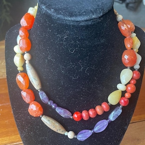 Peut inclure: Un collier à plusieurs rangs composé de perles de formes et de tailles variées. Le collier comprend de la cornaline orange à facettes, des pierres jaune pâle lisses, des perles cylindriques beige moucheté, des perles rouges et de l'améthyste.