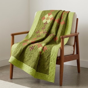 May include: A quilted throw blanket in shades of olive and lime green featuring a repeating geometric block pattern with small red and orange accents. The fabric has an all-over swirling stitched texture and a solid lime green border trim.