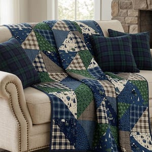 May include: A patchwork quilt featuring triangular segments in navy blue, forest green, and tan plaid, alongside cream fabric printed with small blue sailboats and trees. Three matching square throw pillows in a dark navy and green plaid pattern.