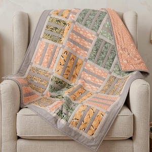 May include: A patchwork quilt featuring a grid of rectangular fabric panels in shades of sage green, soft peach, and mustard yellow. The quilt displays various patterns including botanical leaves, clouds, and abstract shapes, finished with grey borders.