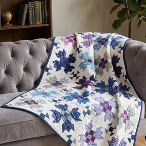 May include: A quilted blanket featuring a repeating star pattern in shades of blue, purple, and green on a white background. The quilt has a dark blue fabric border and visible stitching throughout, creating a textured surface across the fabric.
