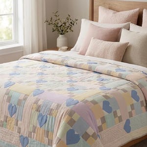 May include: A patchwork quilt featuring a grid of pastel-colored squares in shades of yellow, blue, pink, and green. The quilt is decorated with multiple blue fabric heart appliques stitched onto the surface, creating a repeating pattern across the fabric.