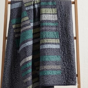 Draped patchwork bed quilt showing teal, sage, and cream diagonal strip design