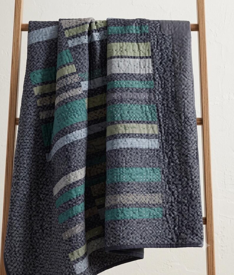 Draped patchwork bed quilt showing teal, sage, and cream diagonal strip design