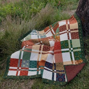 May include: A patchwork quilt featuring a variety of geometric and floral patterns in shades of rust orange, forest green, cream, and brown. The quilt is constructed from square blocks with a dark green border and a solid brown fabric backing.
